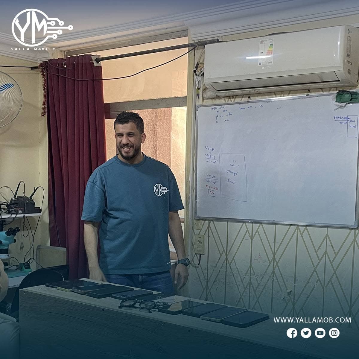 مدرب يلا موبايل يقف بجانب طاولة تحتوي على أجهزة حقيقية أثناء شرح نظري